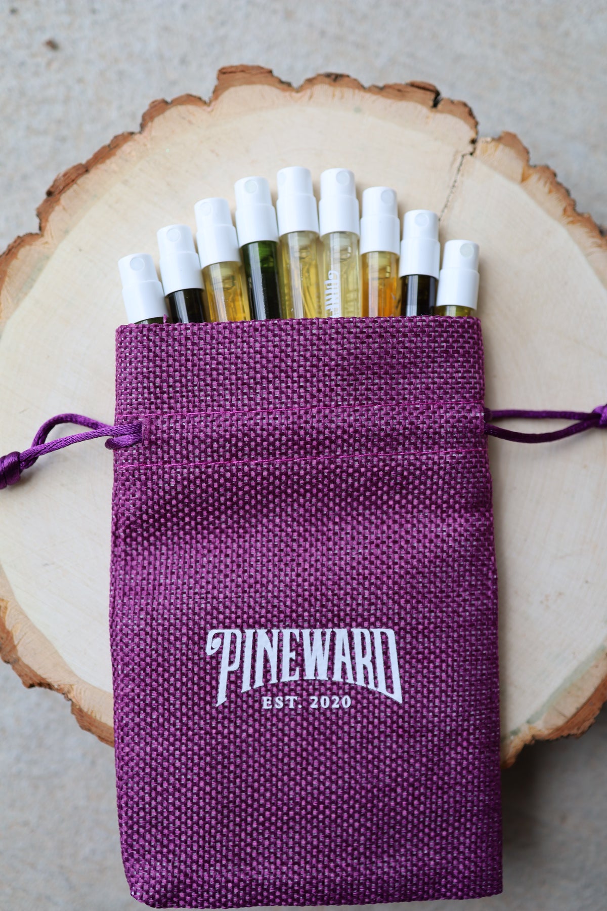 Purple drawstring pouch with DINEWARD logo, filled with fragrance oil bottles
