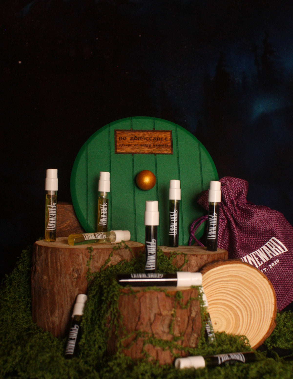 Rustic gift set with bottles, red drawstring pouch, wood logs, and moss circle backdrop